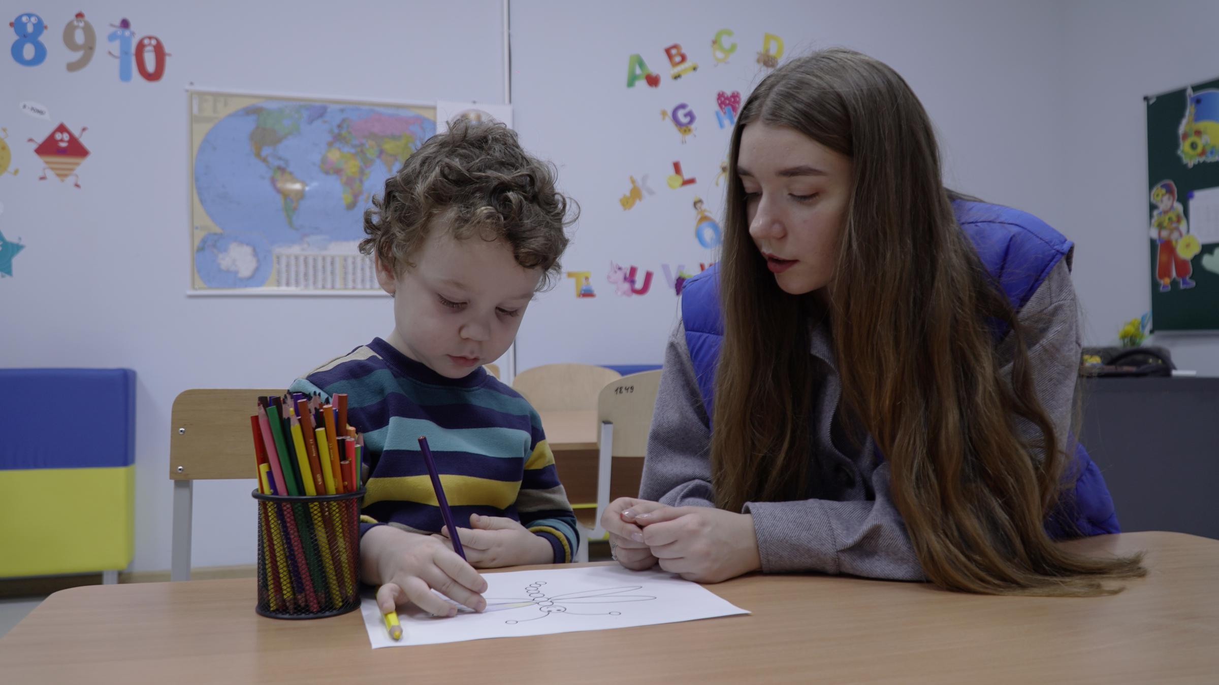 Kind malt in Begleitung von Lehrpersonal. Die Kindernothilfe und ihre Partner unterstützen Kinder mit ergänzenden Bildungsangeboten und psychosozialer Hilfe (Foto: Myrne Nebo – Peaceful Heavens of Kharkiv)