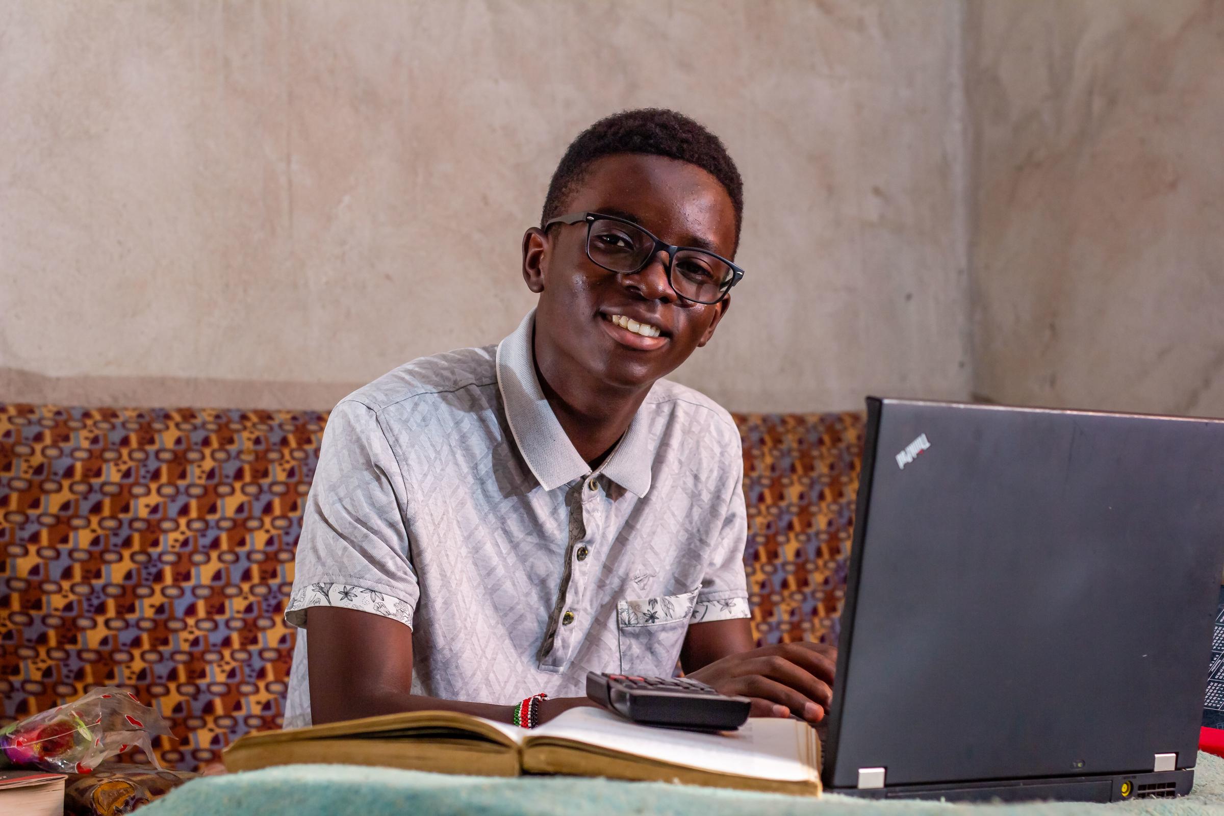 Junge sitzt am Laptop und lächelt in die Kamera (Quelle: Kindernothilfe)