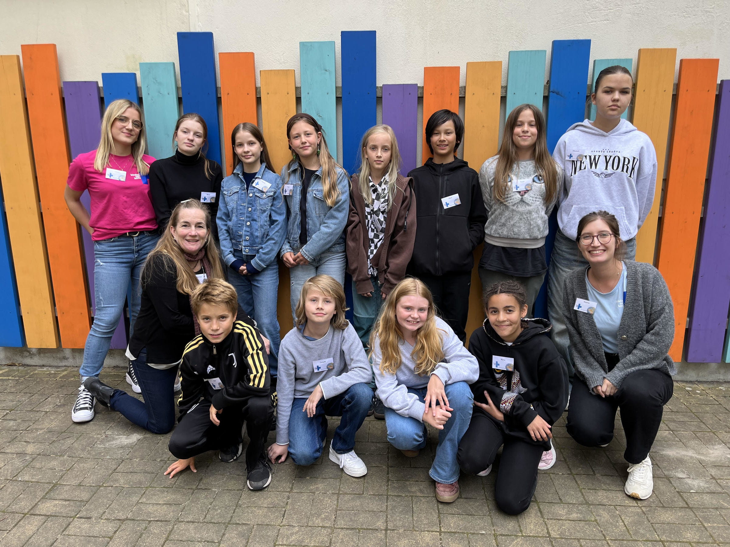 Gruppenfoto von Mädchen und Jungen und zwei Kindernothilfe-Mitarbeiterinnen vor einer bunten Wand (Quelle: Kindernothilfe)