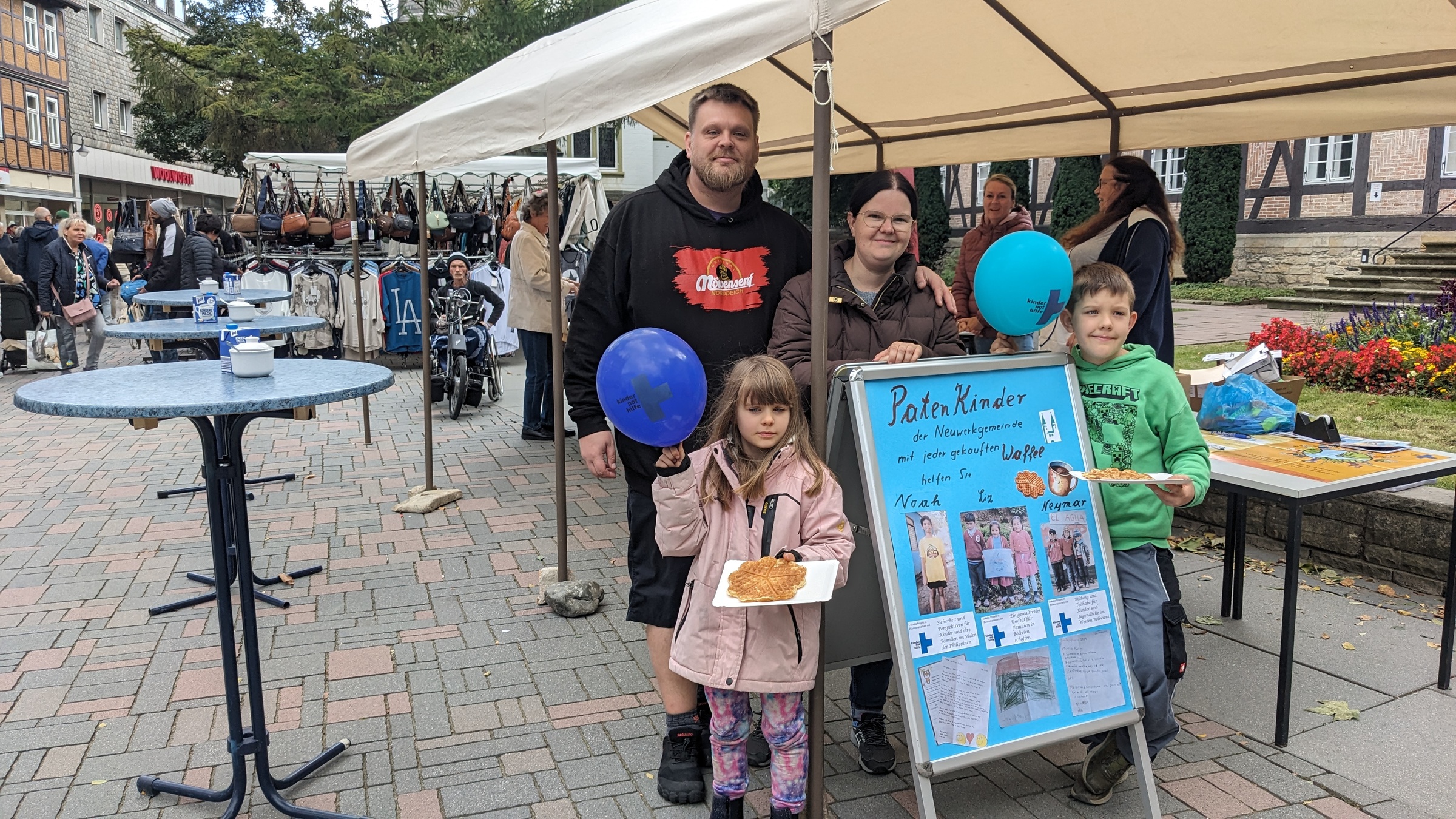 Ein Waffelstand, davor eine Familie mit einem selbst gemalten Plakat (Quelle: privat)