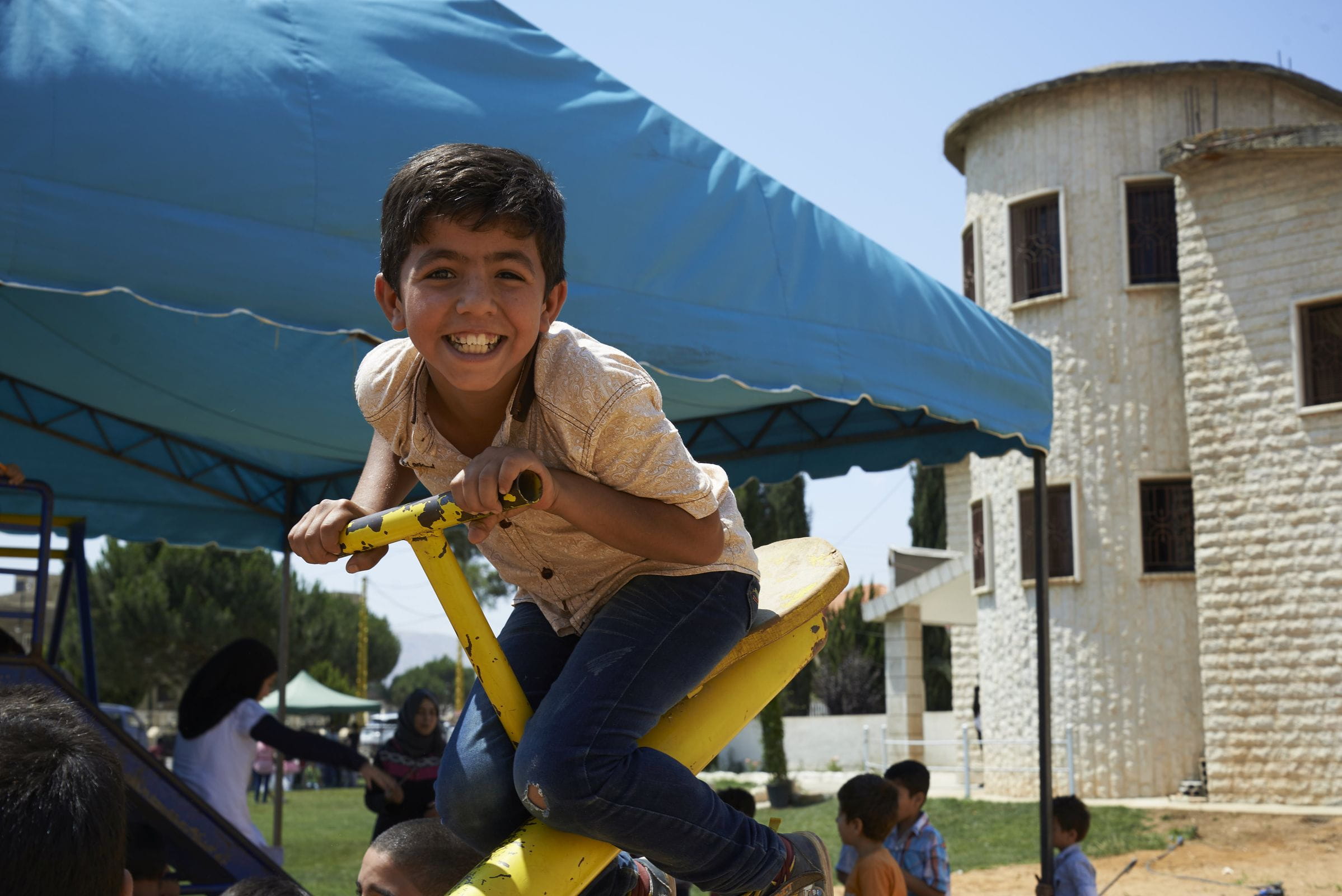 Reportage Libanon; Foto: Kind auf Wippe lacht in die Kamera (Quelle: Ulrich Gernhardt / Kindernothilfe) Reportage Libanon; Foto: Kind auf Wippe lacht in die Kamera (Quelle: Ulrich Gernhardt / Kindernothilfe)